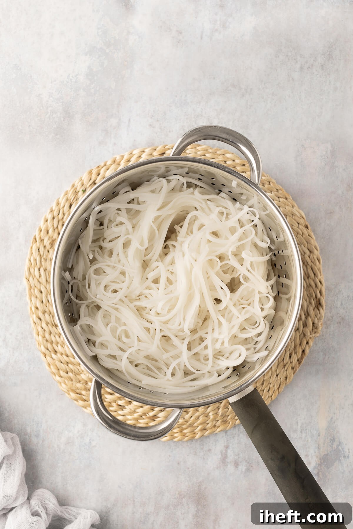 Cooked rice noodles being strained into a colander over a bowl to carefully reserve the cooking liquid, an essential step for the sauce.