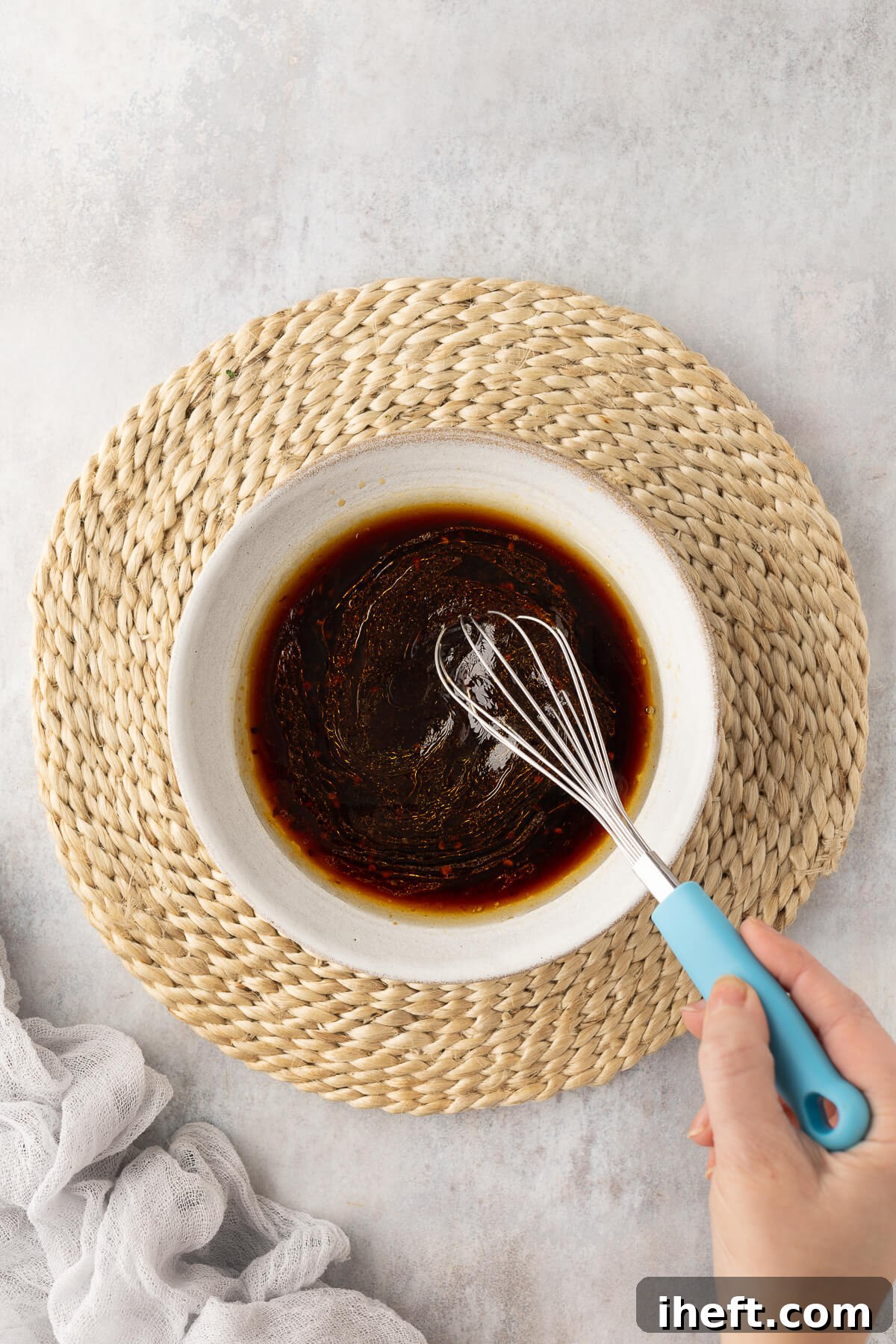 A vibrant Asian chili garlic sauce is expertly whisked together in a pristine white ceramic bowl, showcasing its rich color and smooth consistency, ready for cooking.