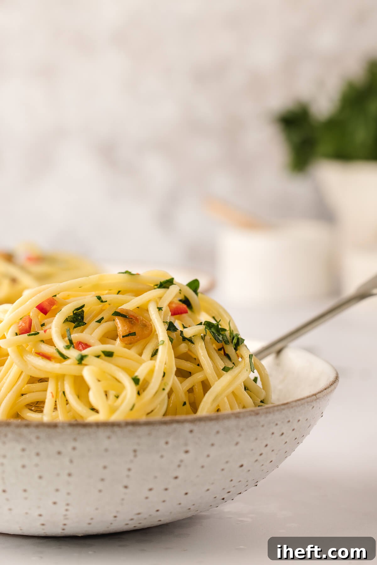 A neutral ceramic bowl filled with homemade Spaghetti Aglio Olio e Peperoncino topped with parsley. 