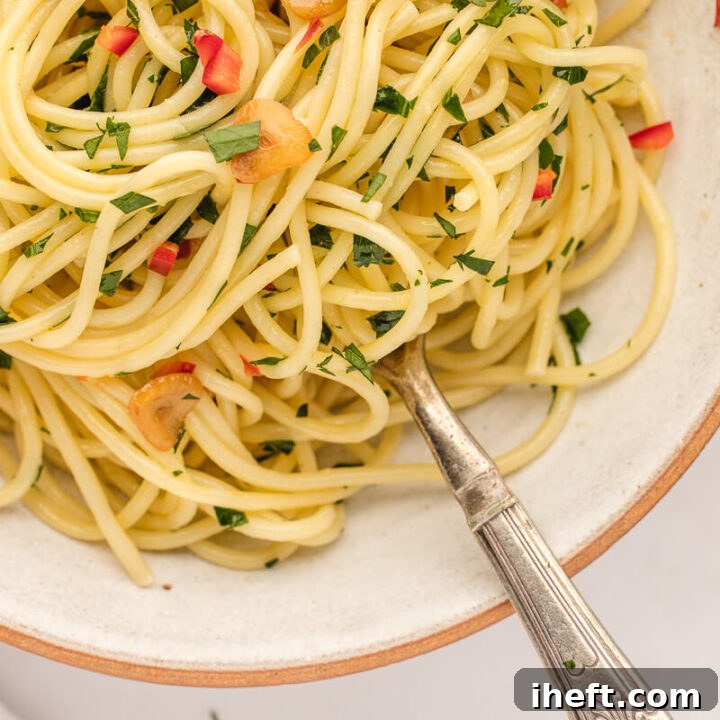 A close-up photo of spaghetti aglio olio e peperoncino in a white ceramic bowl.