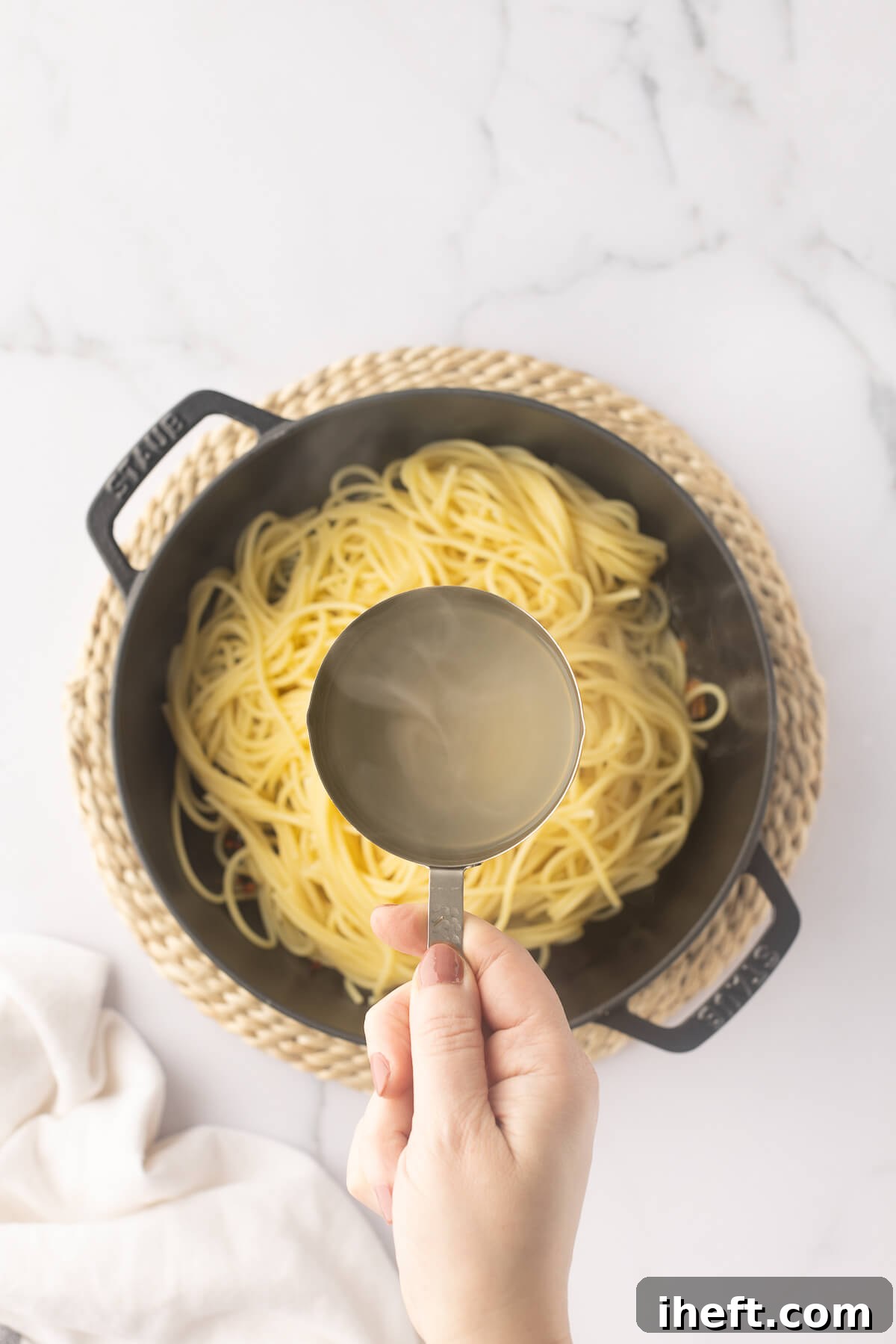 Pasta water is added to a pot of cooked spaghetti.
