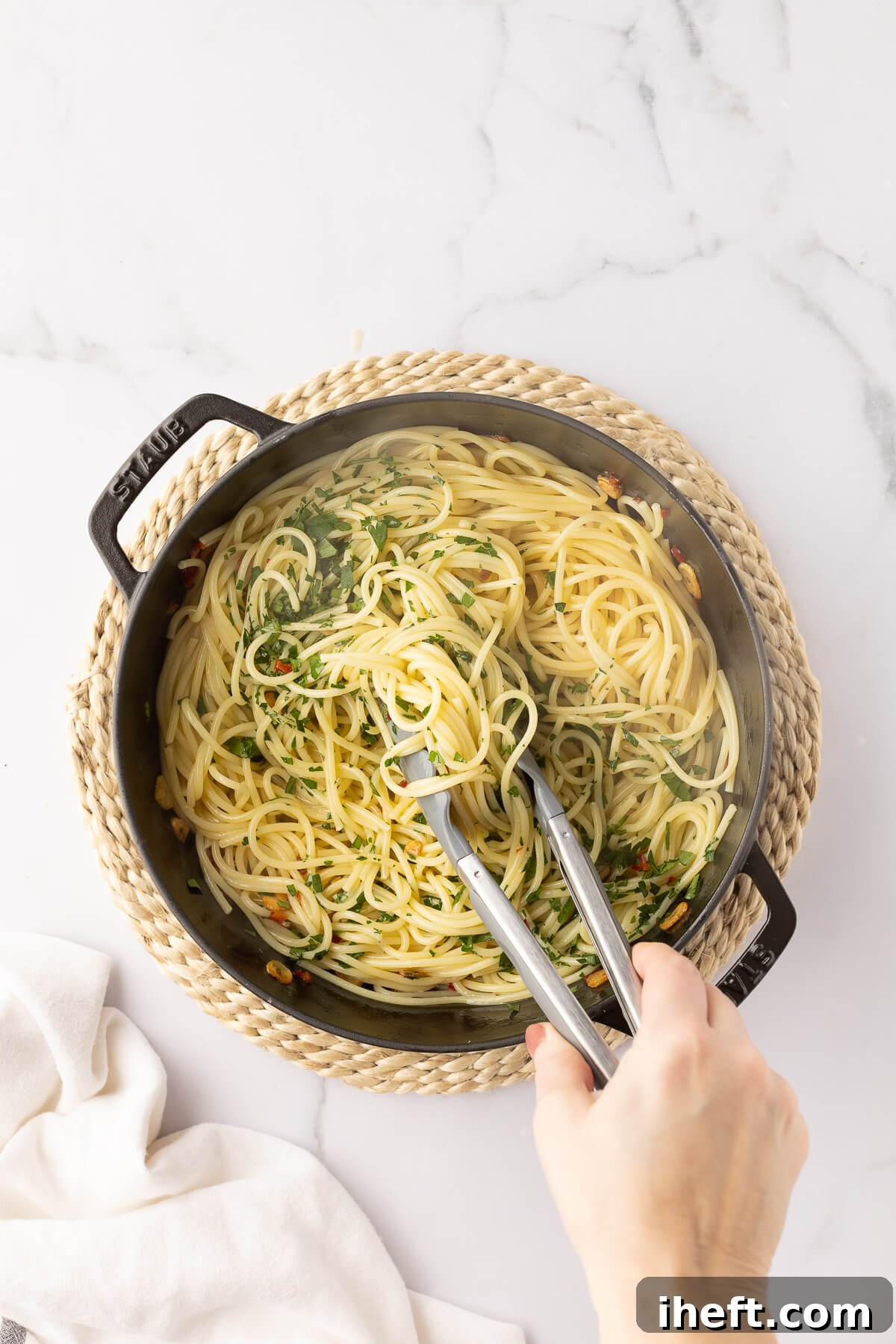 Tongs toss together cooked spaghetti with fresh parsley, olive oil, garlic, and peperoncino.