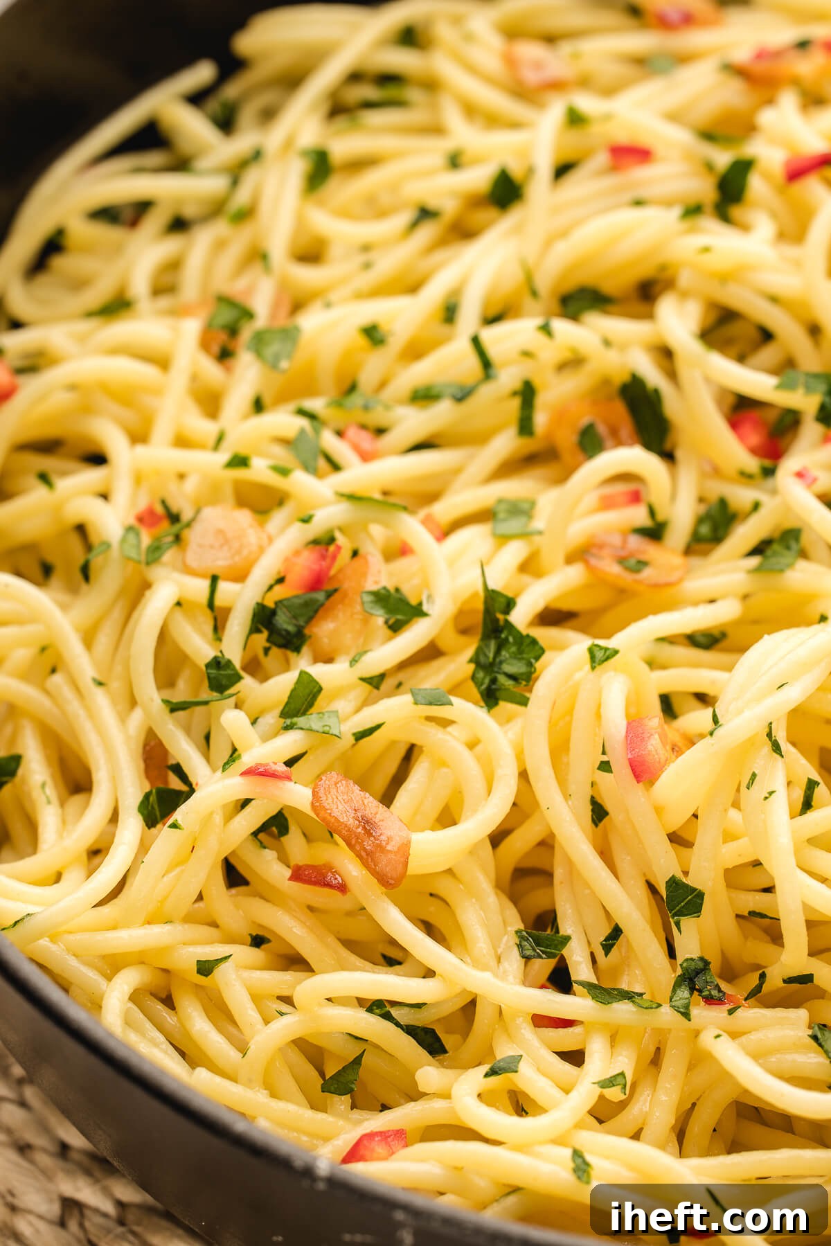A cloes-up photo of spaghetti with sliced garlic, olive oil, and Italian peppers garnished with parsley. 