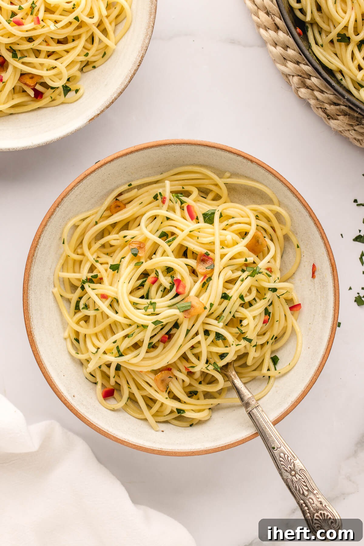 Ceramic pasta bowls filled with Spaghetti Aglio Olio e Peperoncino on a marble countertop. 