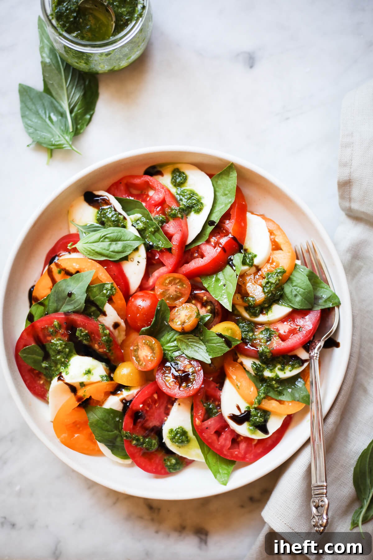 A beautiful plate of Caprese salad made with red and yellow heirloom tomatoes, fresh basil, balsamic and pesto. 