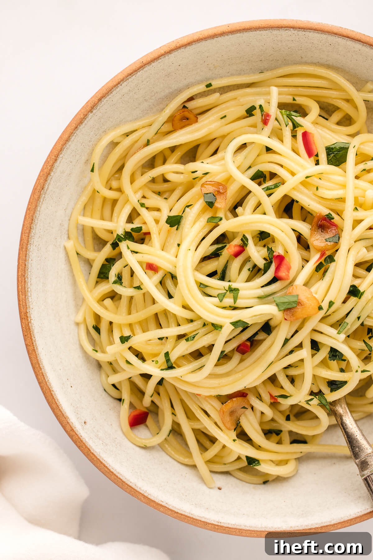 An overhead photo of a ceramic bowl filled with Spaghetti Aglio Olio e Peperoncino garnished with chopped parsley. 