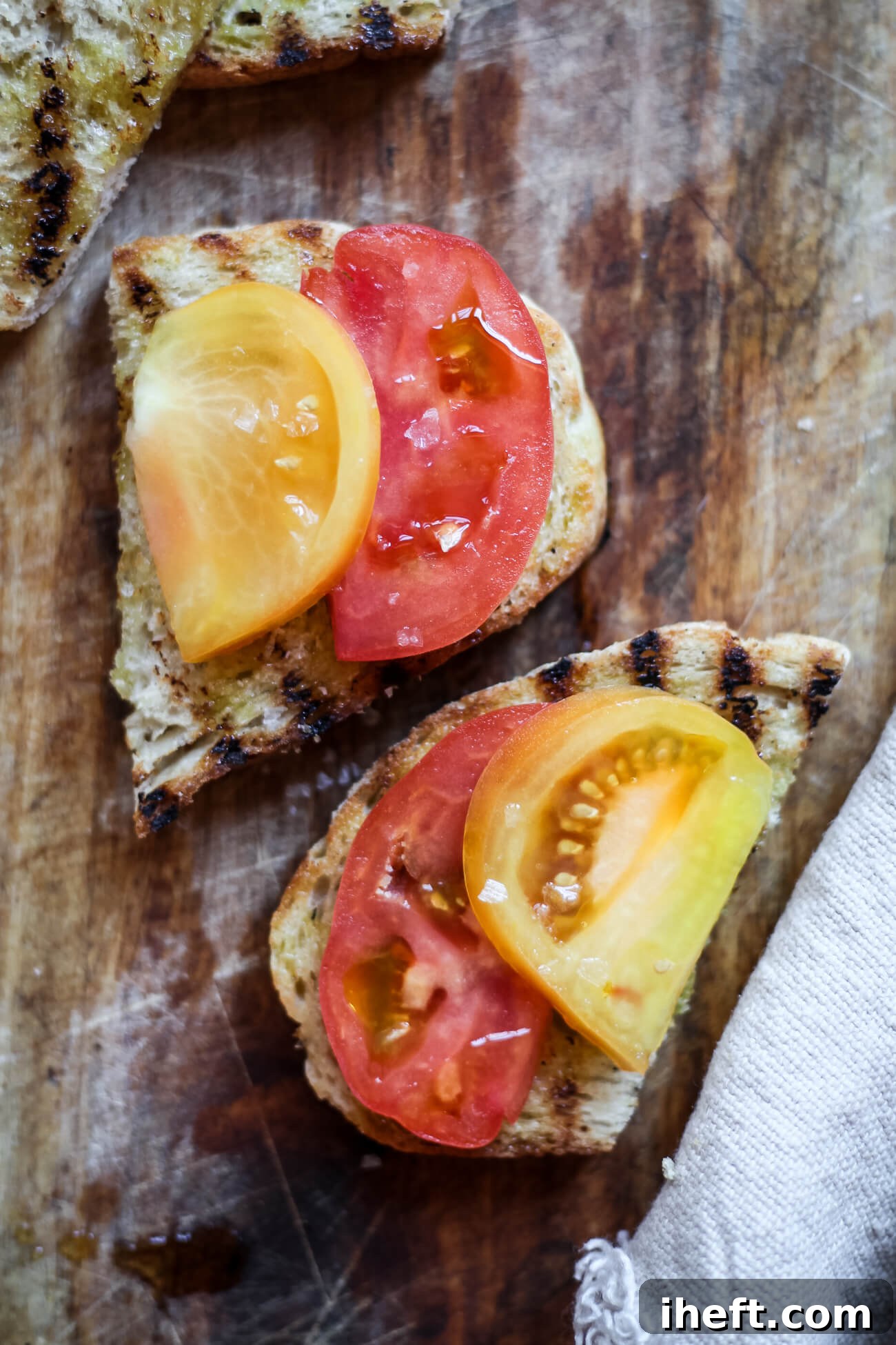 Two slices of grilled Tuscan bread topped with heirloom tomatoes, olive oil, and sea salt.