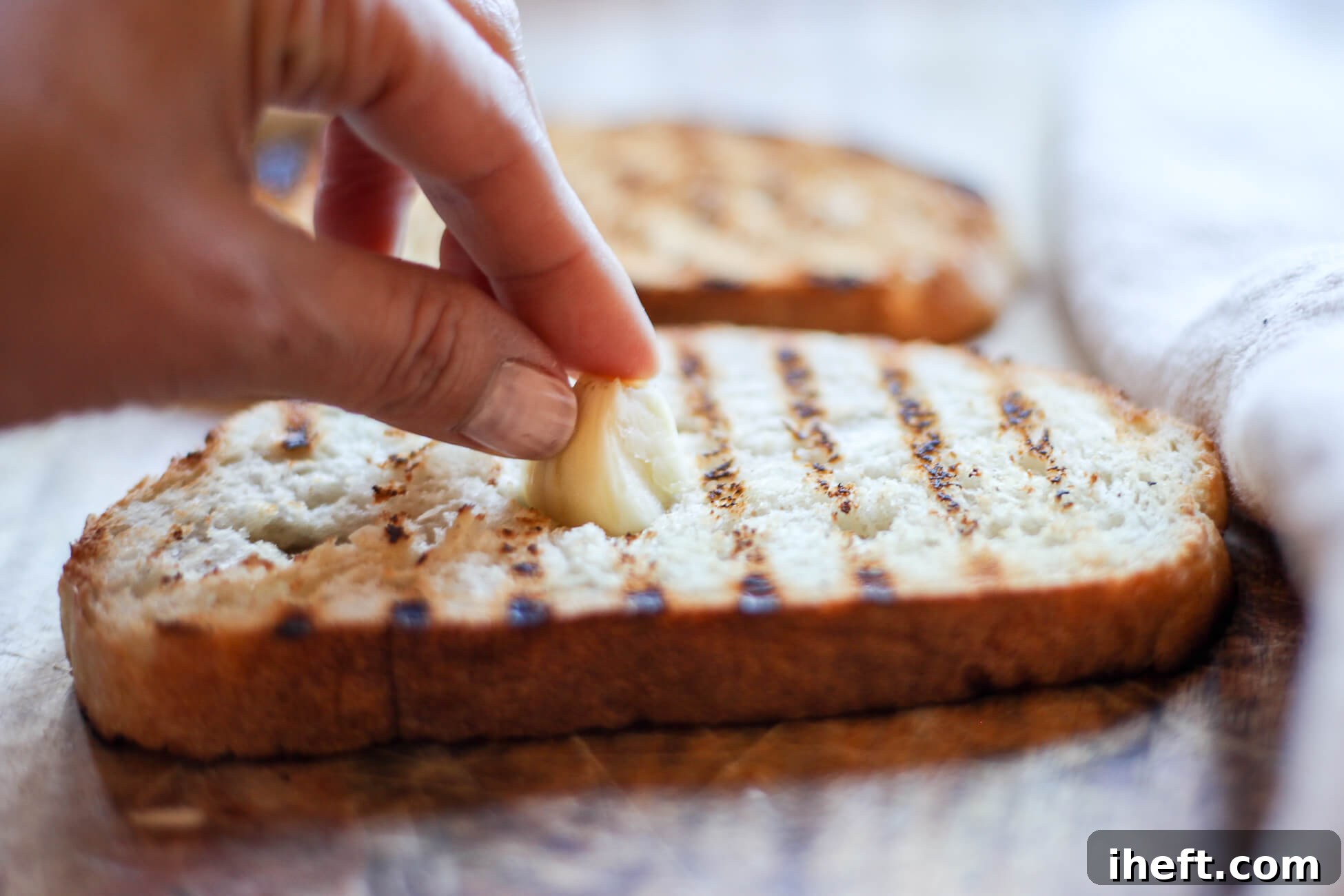 Half of a garlic clove is rubbed over a grilled piece of Tuscan bread bruschetta.