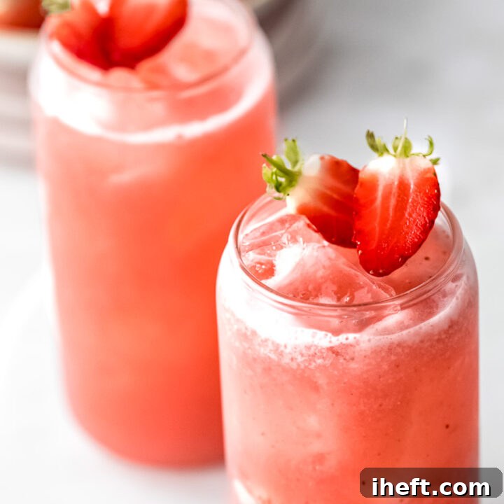 Two tall glasses of strawberry agua fresca (agua de fresa) with ice garnished with halved strawberries.
