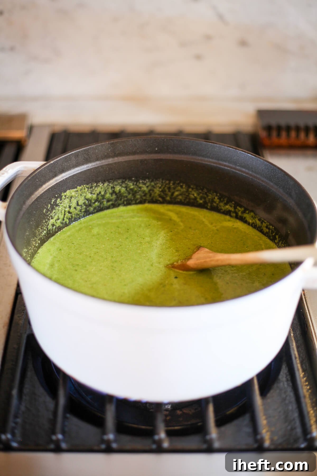 Green pozole verde in a white Staub pot with wooden spoon on a gas burner.