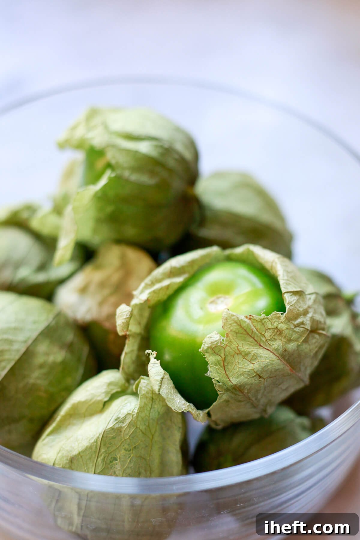 A glass bowl filled with tomatillos in their husks.