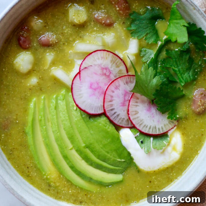 An overhead photo of a bowl of vegetarian pozole verde topped with avocado, radish, sour cream, and cilantro.