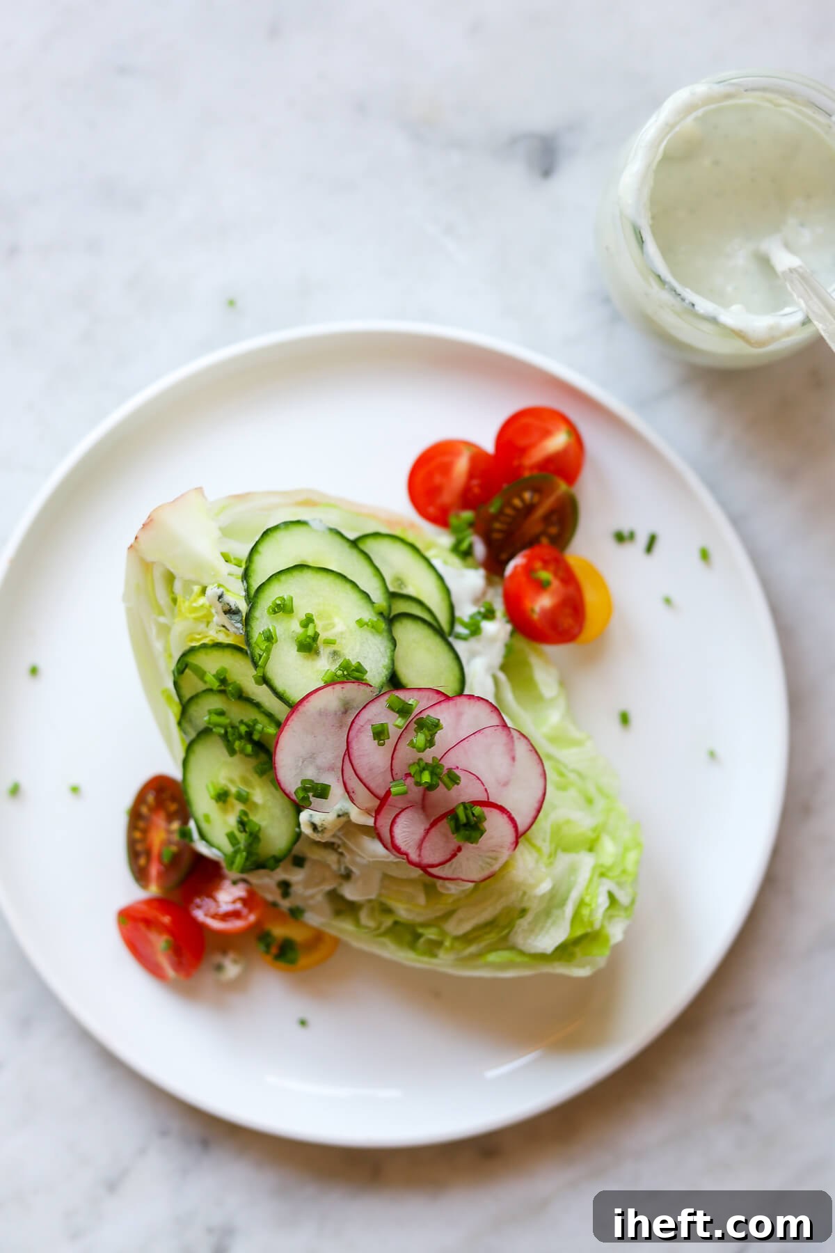 An overhead photo of a wedge salad on a white plate. A small jar of homemade Roquefort blue cheese dressing sits to the side. 