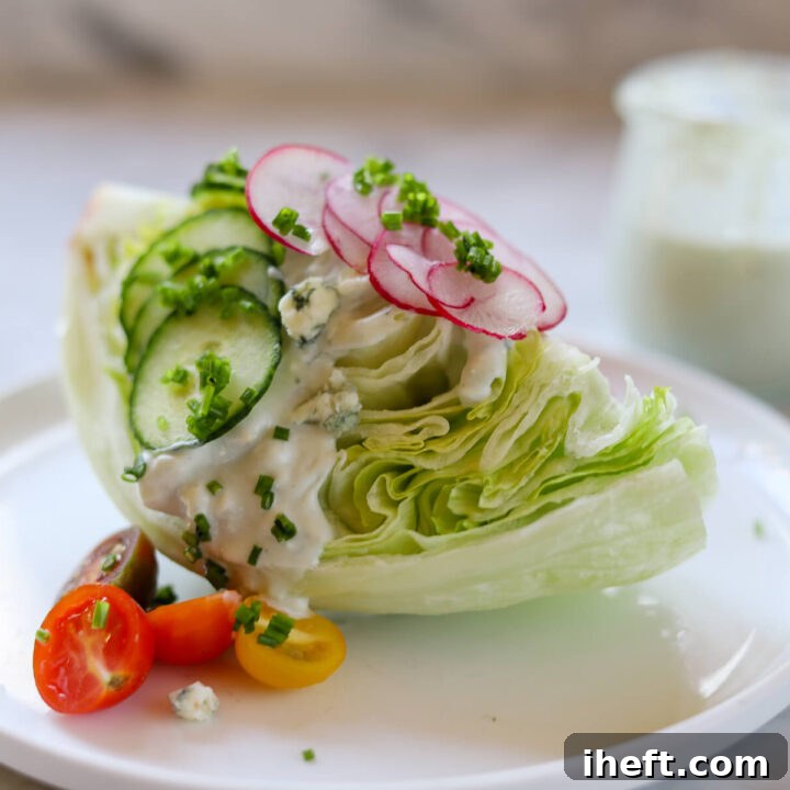 A wedge salad with Roquefort dressing on a white plate. A small jar of homemade blue cheese dressing in the background.