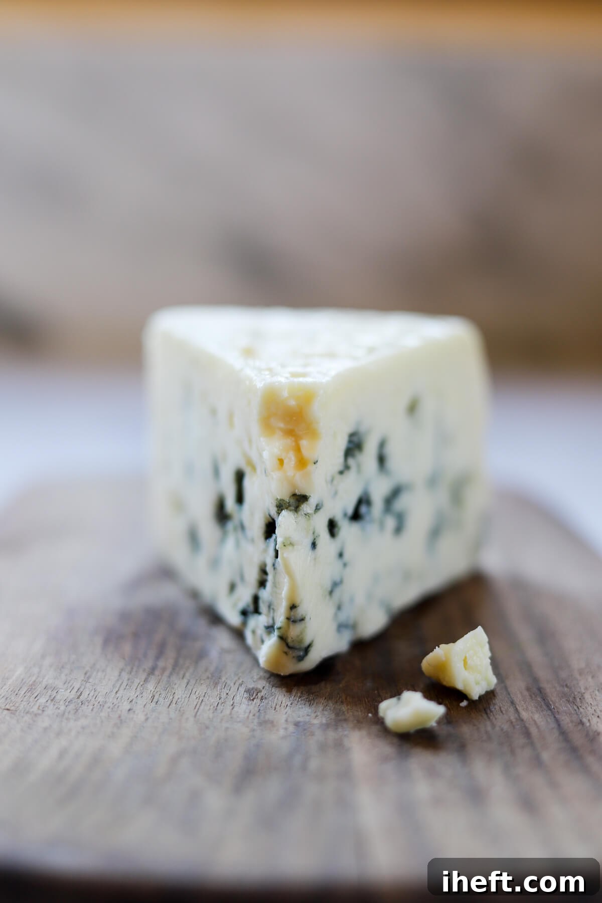 A wedge of Roquefort cheese with crumbles falling off.