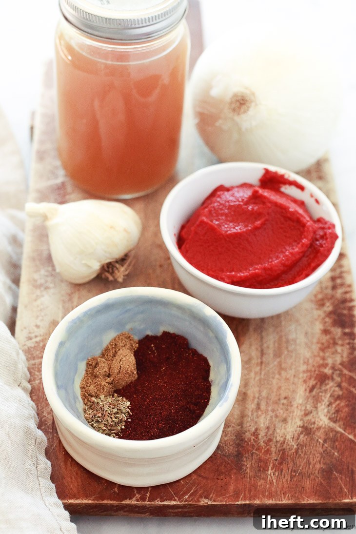 The ingredients for homemade enchilada sauce laid out, including vegetable broth, tomato sauce, garlic, ancho chili powder, cumin, and oregano.