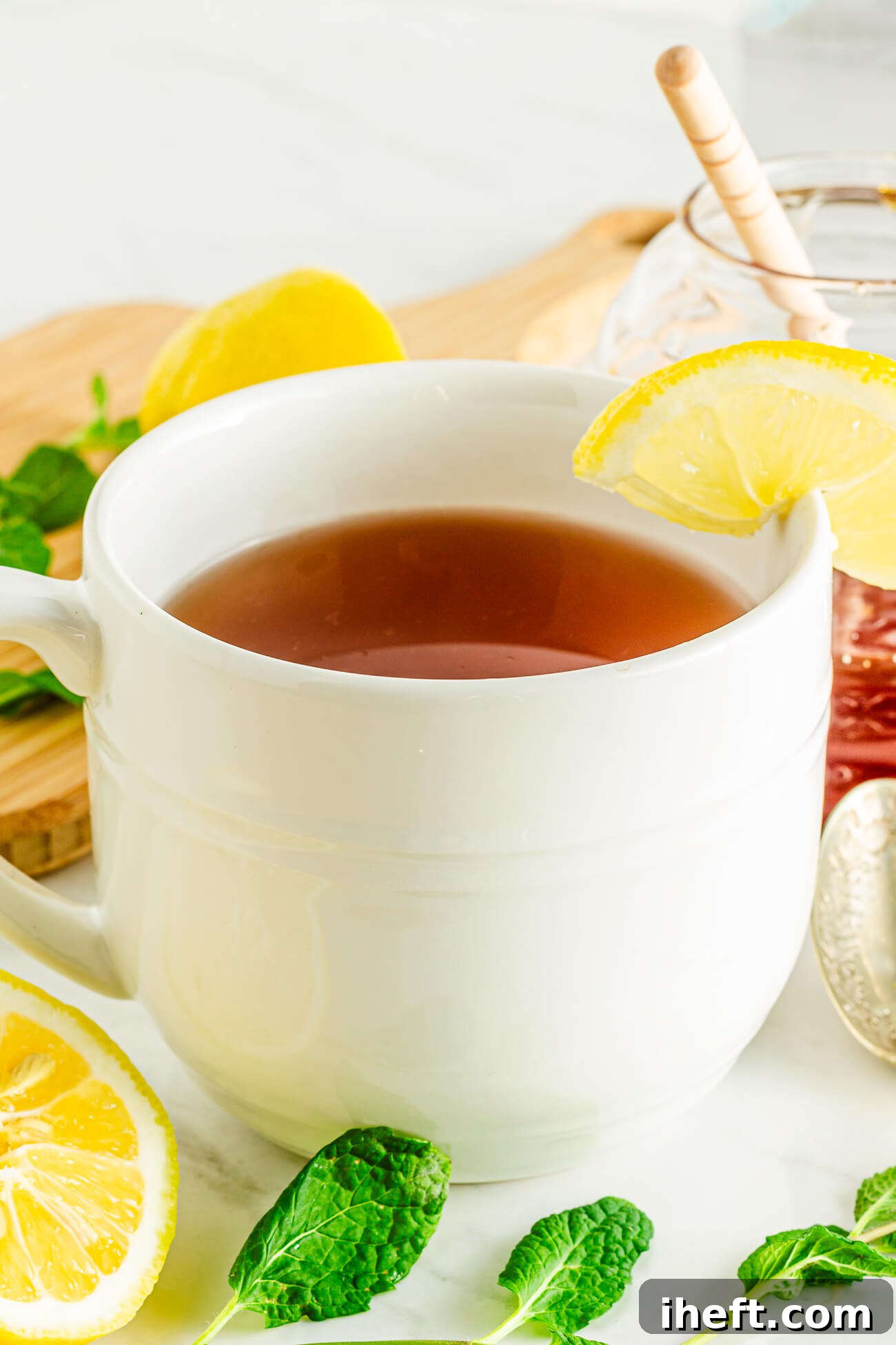 A ceramic mug filled with Honey Citrus Mint Tea made with lemon, honey, and tea bags. The mug is garnished with a lemon slice and fresh mint.