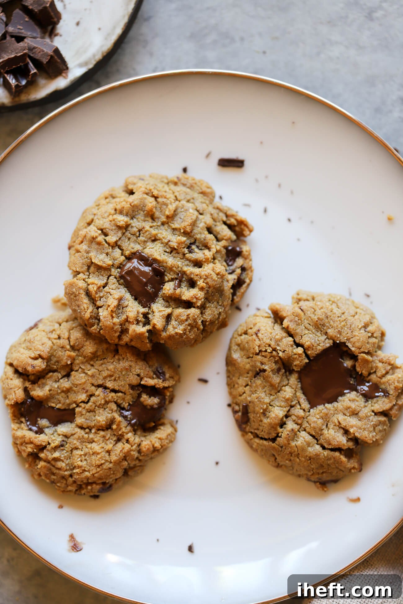 A white plate showcasing three perfectly baked oat flour peanut butter cookies, adorned with generous, melty dark chocolate chunks. These cookies are notably soft, chewy, vegan, and gluten-free.