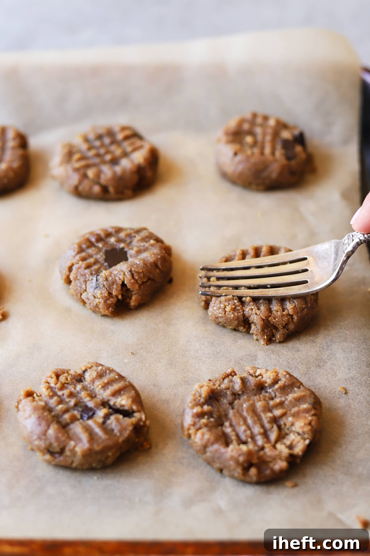 A fork pressing down on peanut butter chocolate chunk cookie dough balls on a cookie sheet, creating the classic pattern.