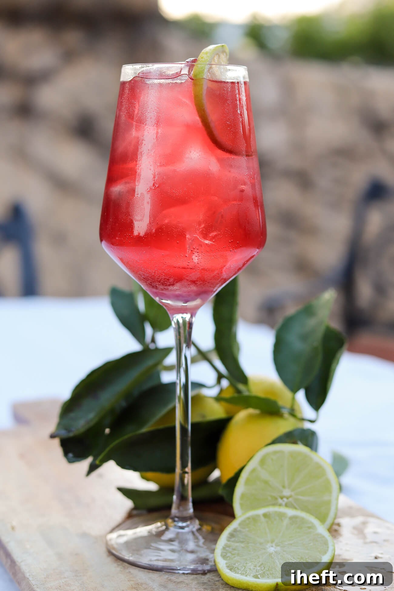 A serene outdoor setting featuring a beautiful red cherry juice and magnesium sleep mocktail, served over ice in a wine glass with a lime garnish on a rustic table.