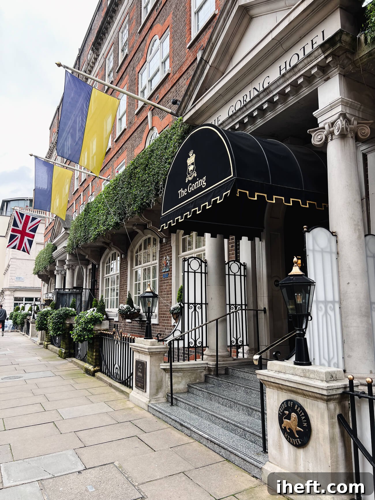 The front of The Goring hotel in Belgravia. The facade is a brick building with green plants, flags, and a black arched covering that say "The Goring" in gold writing. 