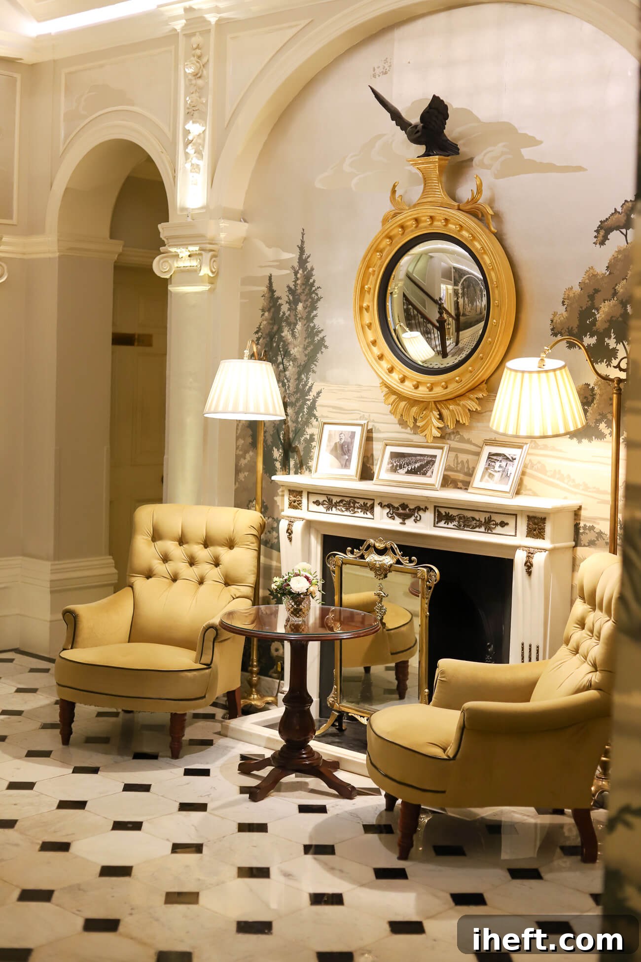 A beautiful sitting area with two chairs and a table in front of a fireplace and hand-painted wallpaper at the Goring Hotel in Belgravia London. 