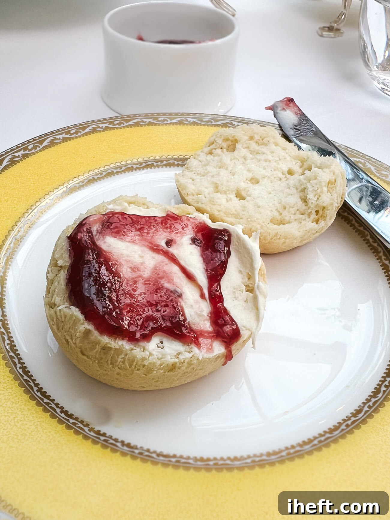 A classic British scone, freshly baked and halved, generously adorned with luscious Devonshire clotted cream and The Goring Hotel's homemade jam, captured in a mouthwatering photo during afternoon tea in London.