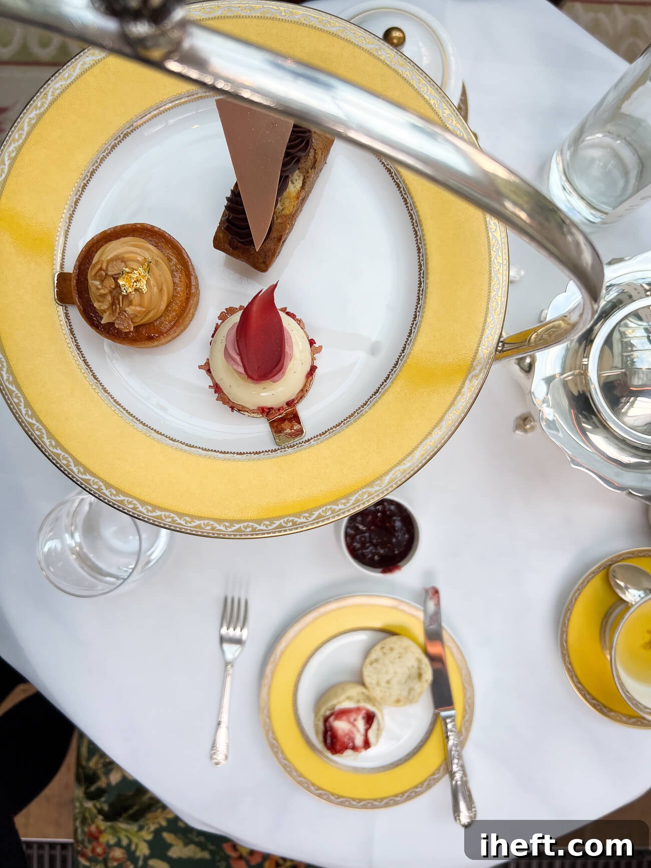 An elegant overhead photograph showcasing the complete afternoon tea spread at The Goring Hotel in London. The top tier features three exquisitely presented desserts, while a scone adorned with clotted cream and jam rests on a pristine table, creating a luxurious and inviting scene that highlights why this is considered the best afternoon tea in London.