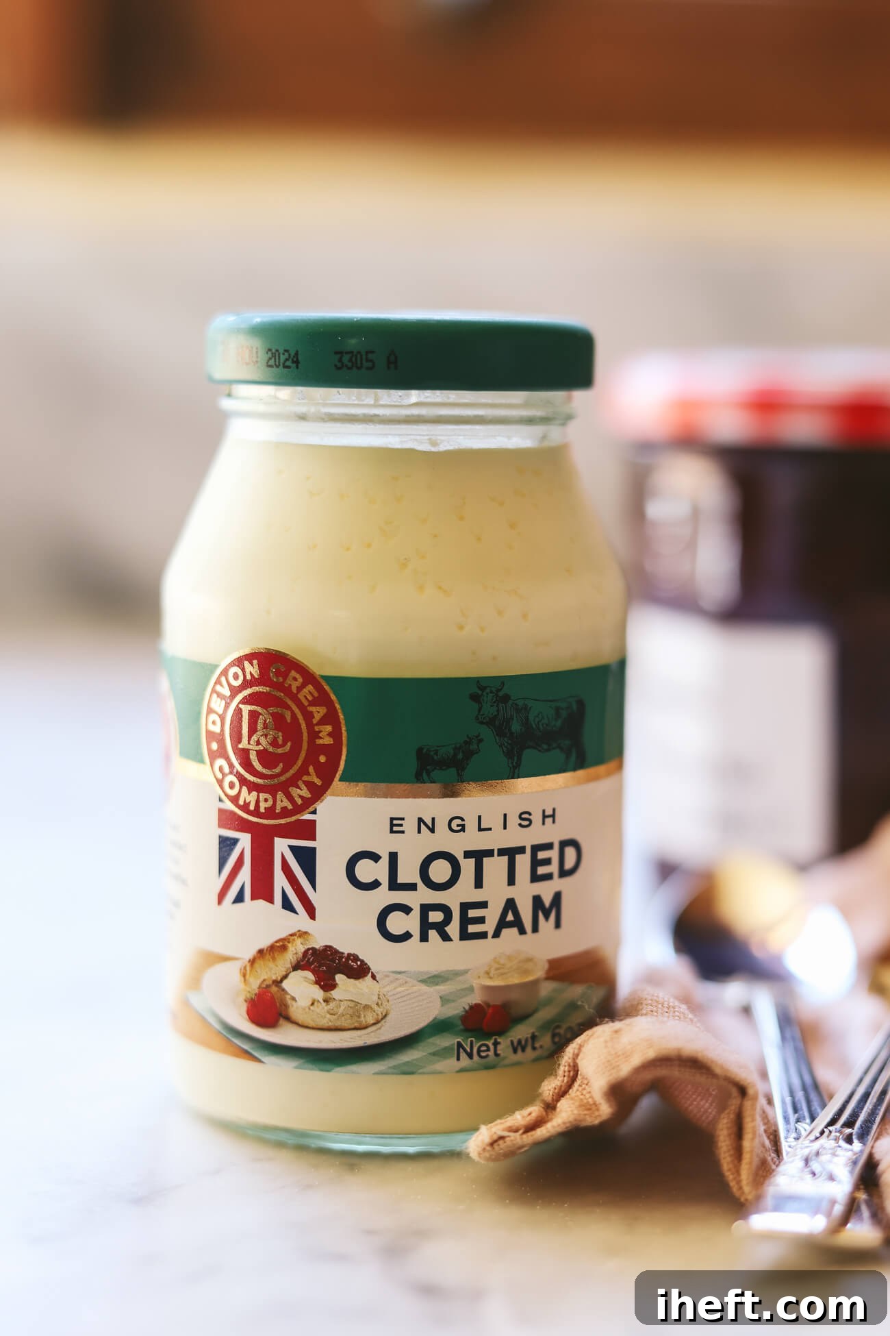 A charming glass jar of authentic English clotted cream stands on a gleaming marble countertop. The label clearly displays "Devon Cream Company," emphasizing its traditional origin and quality.