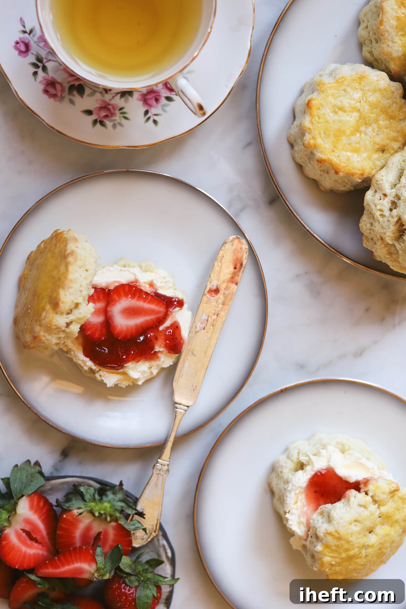 An inviting overhead photo of a homemade cream tea, featuring perfectly plain butter scones generously topped with rich clotted cream and strawberry jam, served with fresh strawberries and a delicate cup of English tea.
