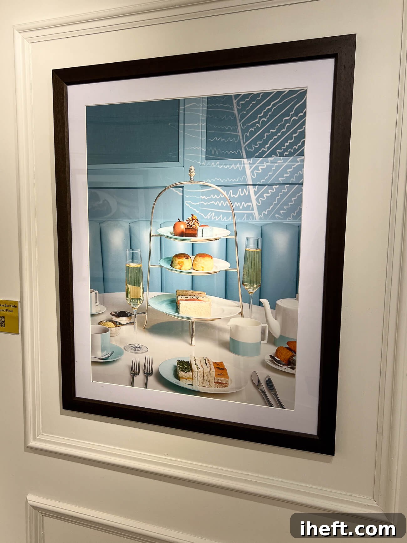 A vibrant poster at Harrods in London advertising their renowned afternoon tea, featuring an enticing display of scones, finger sandwiches, and elegant desserts on a tiered stand, complemented by champagne and tea.