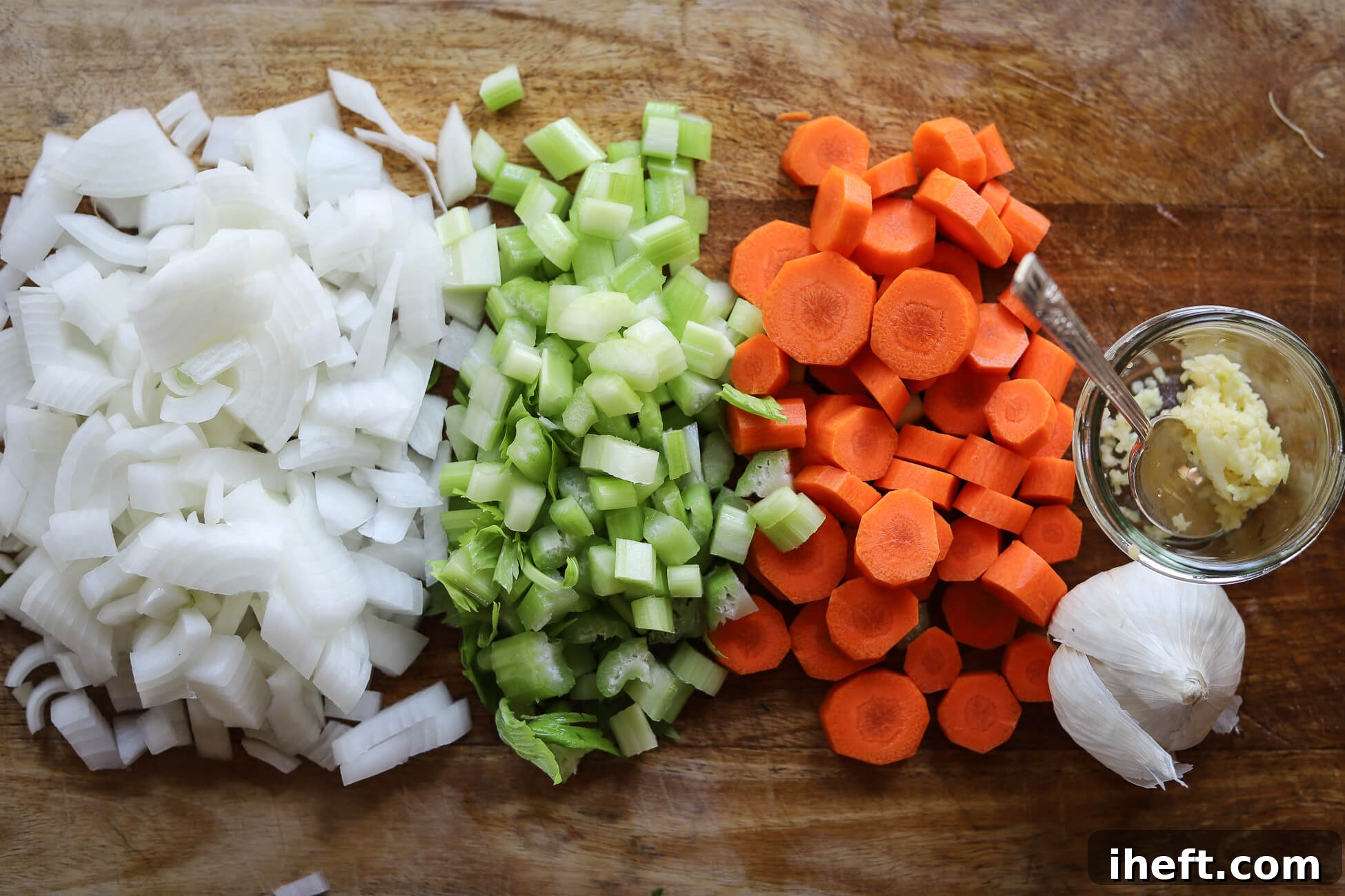 Chopped wh ite onion, celery, sliced carrots, and crushed garlic on a wooden cutting board to prep for Greek bean soup. 