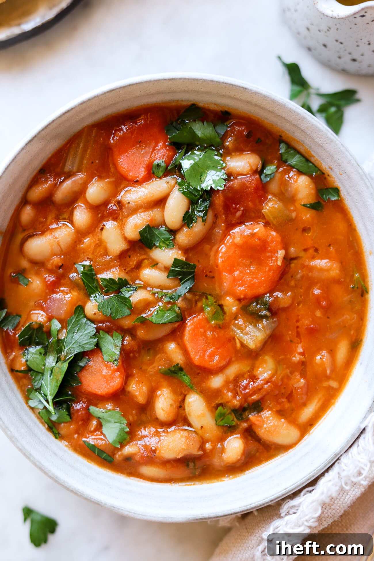 An overhead close-up photo of Greek bean soup with carrots and parsley. 