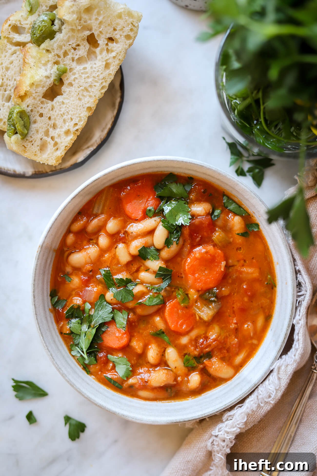 An overhead photo of Greek white bean soup in a bowl with olive focaccia on the side. A simple Blue Zone dinner recipe. 
