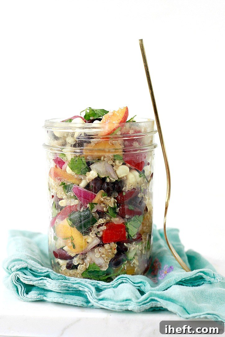 A colorful and hearty vegan quinoa salad, brimming with fresh summer ingredients like sweet corn, robust black beans, succulent peaches, crisp cucumber, and creamy avocado, presented beautifully in a large serving bowl.