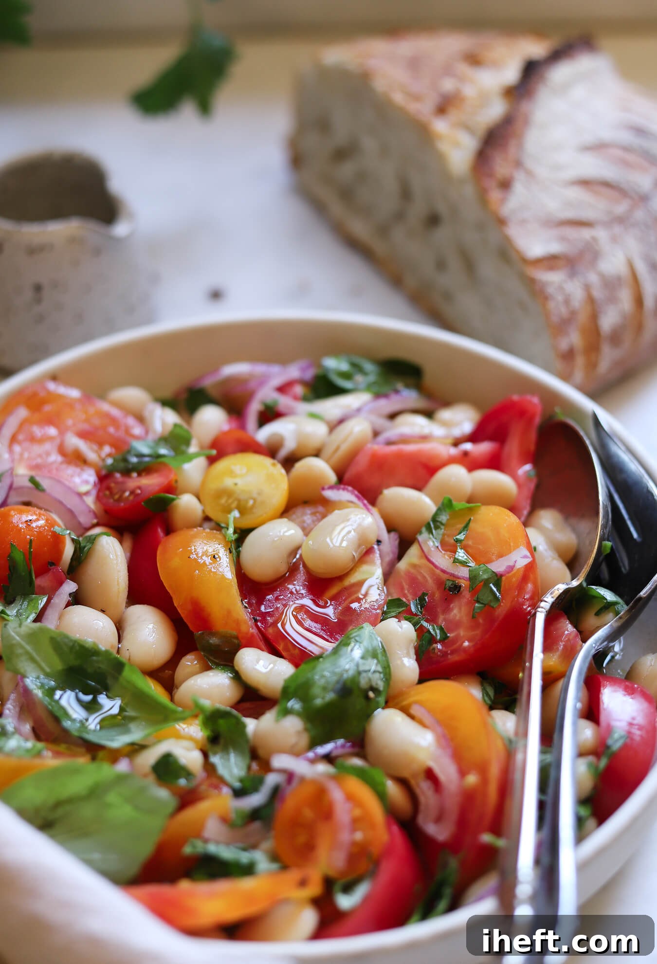 A ceramic rimmed dish filled with a healthy white bean salad made with butter beans, tomatoes, basil, and sliced red onion. 