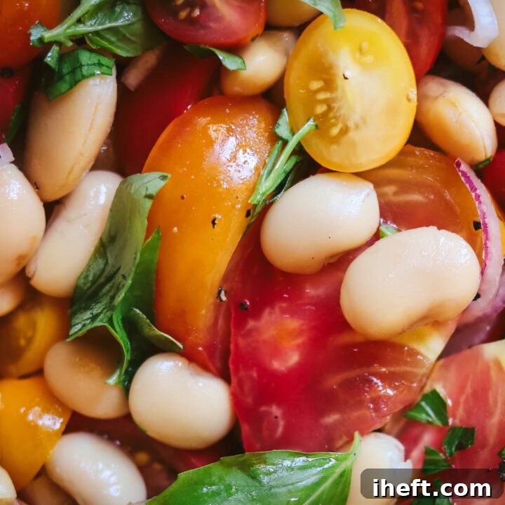 Close-up photo of a butter bean and tomato salad with fresh basil and parsley. The tomatoes are red and yellow heirloom tomatoes.