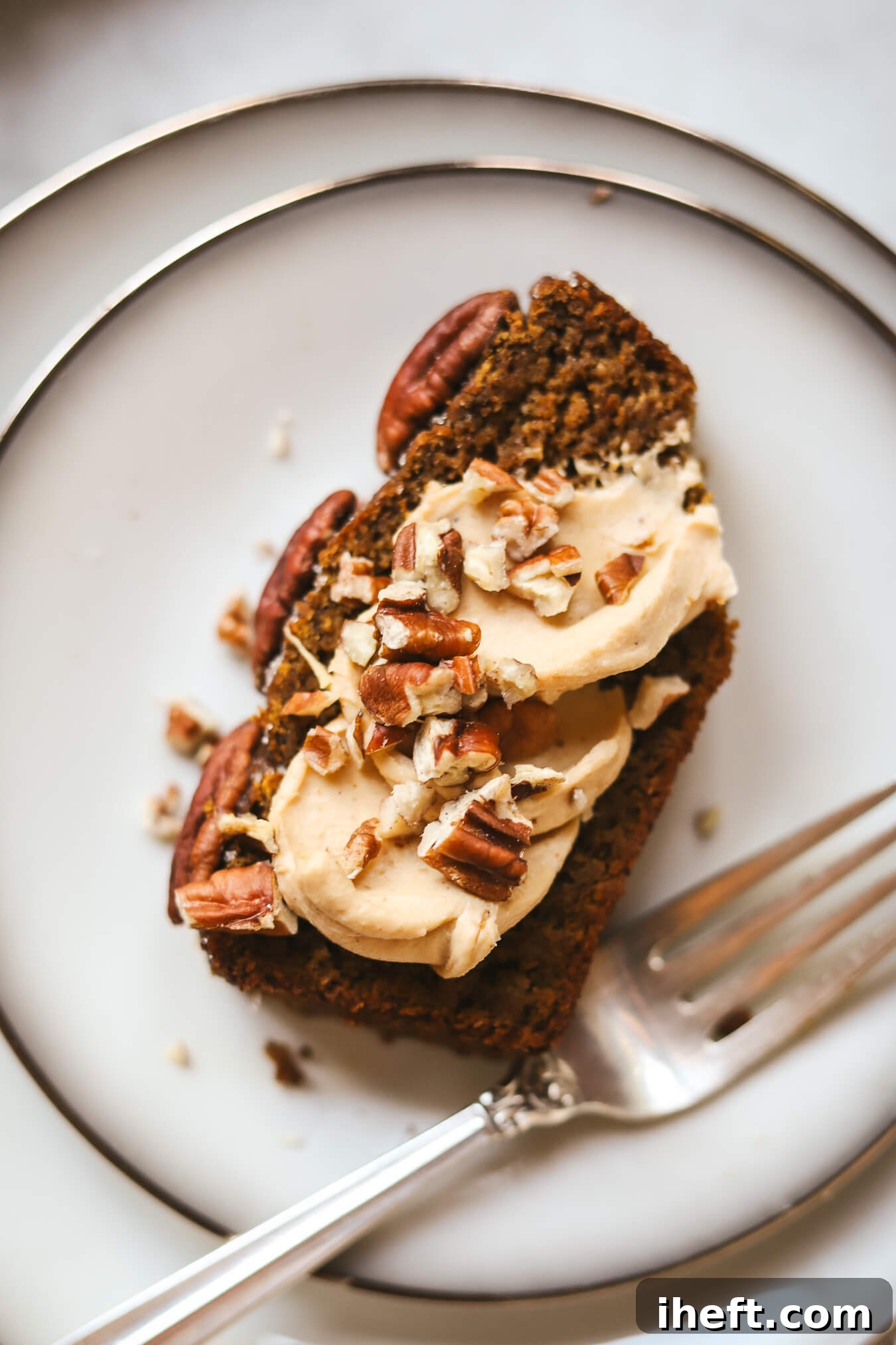A slice of healthy gluten free pumpkin bread made with almond flour on a white plate. The slice is topped with pumpkin cream cheese and pecans. 