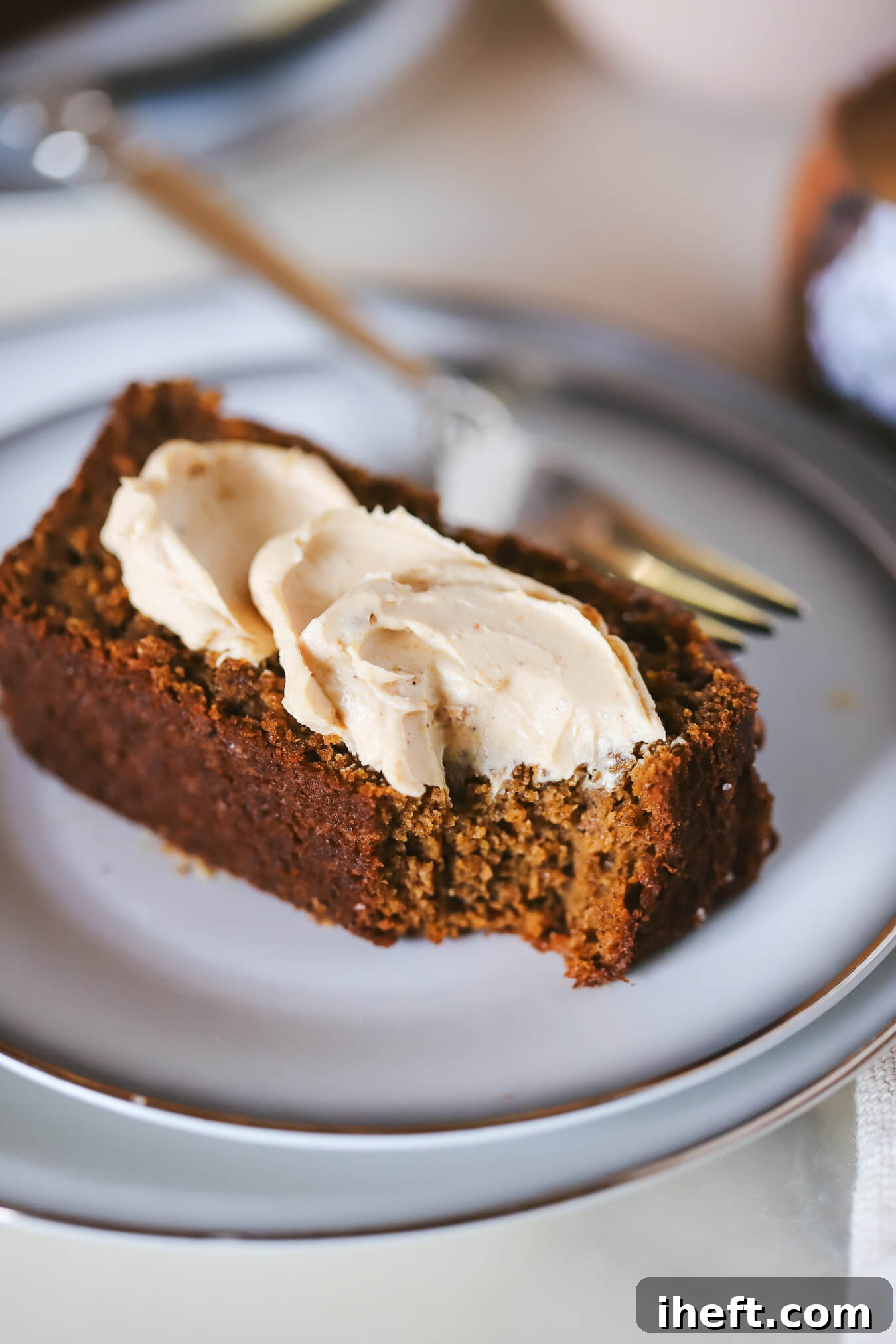 A slice of healthy paleo pumpkin bread topped with Trader Joe's pumpkin cream cheese on a white plate with a gold fork. 