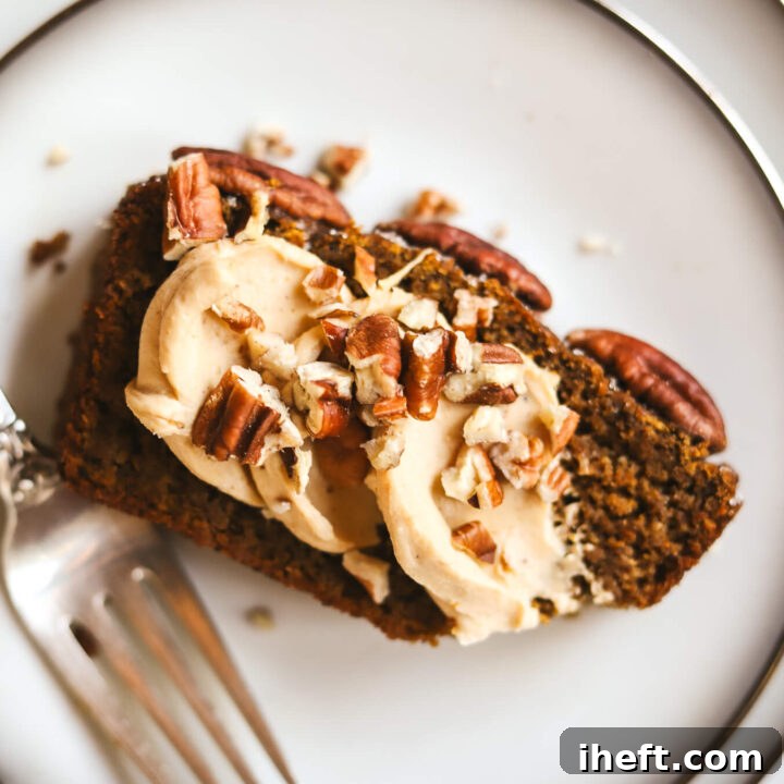 A slice of healthy gluten free pumpkin bread on a white plate topped with pumpkin cream cheese and pecans.