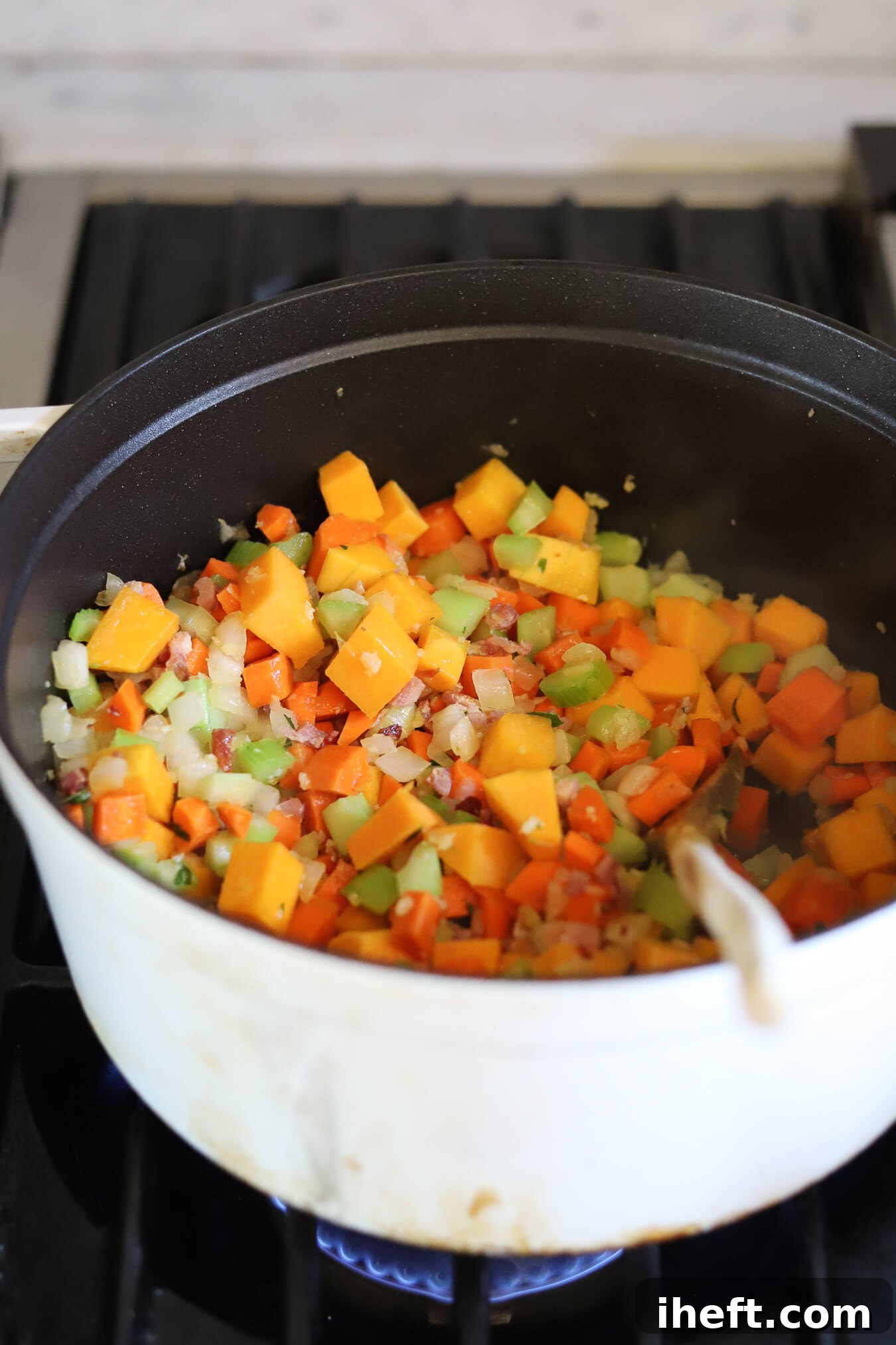 Vegetables and pancetta saute in a white Staub pot while. making Ina Garten's Winter Minestrone Recipe. 