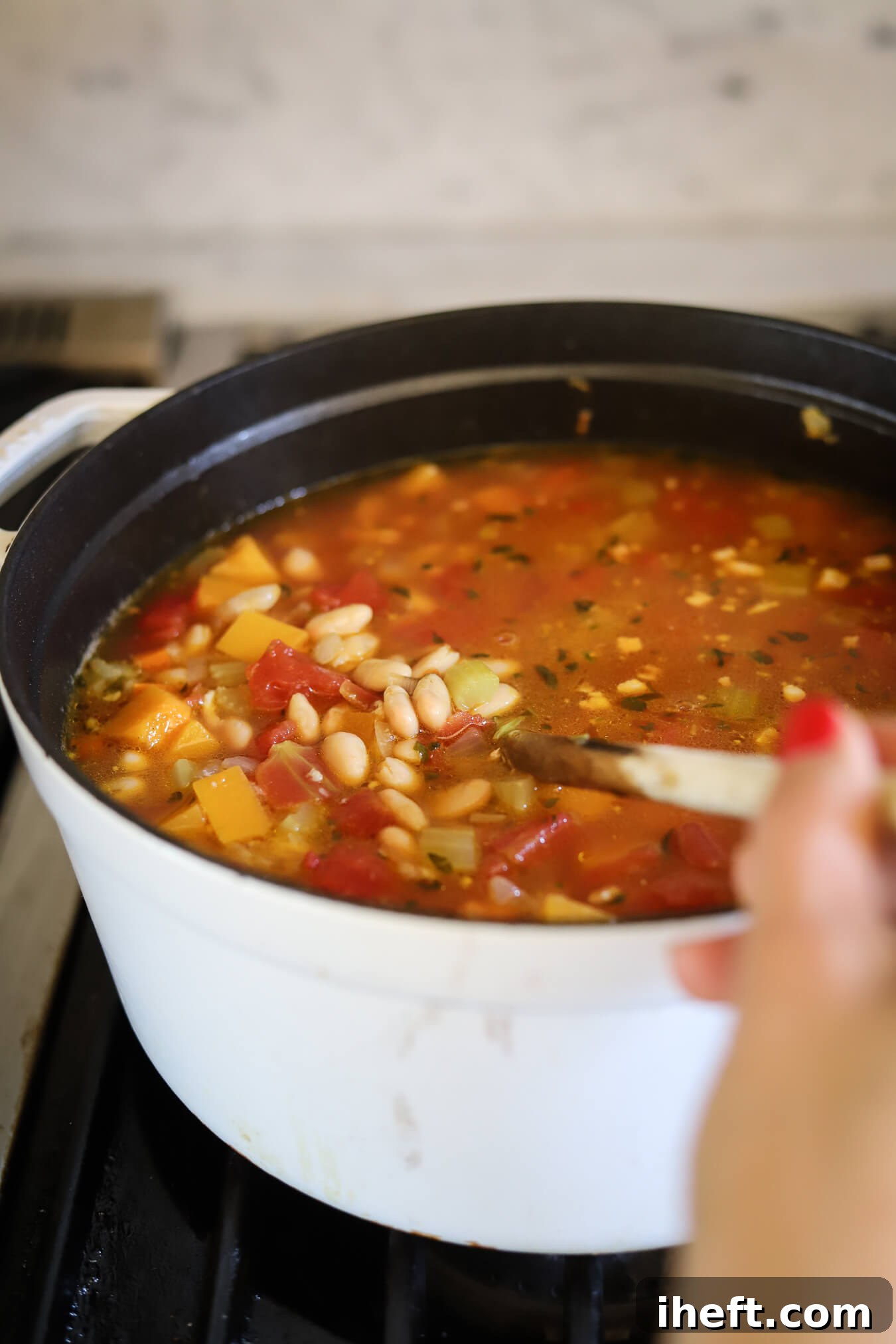 Winter minestrone with white beans and butternut squash simmers in a white pot on the stove. This is a classic Barefoot Contessa recipe. 
