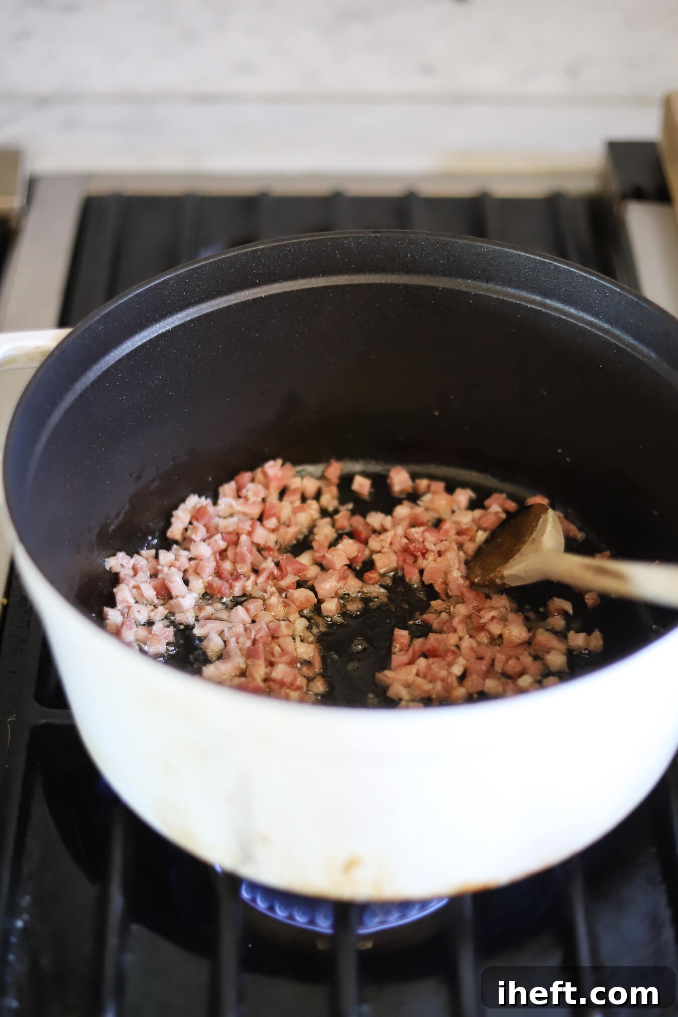 Diced pancetta is sauteed in a white Dutch oven on the stove.