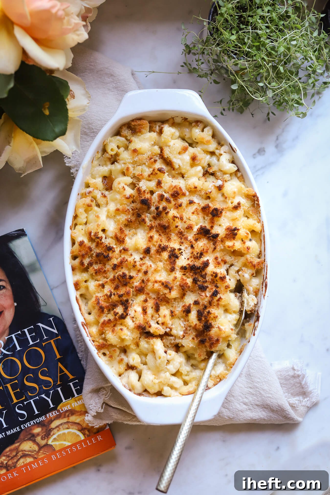 An overhead photo of Ina Garten Mac and Cheese made in a white oval casserole dish. This is a baked mac and cheese with crispy breadcrumb topping. Ina's cookbook can be seen off to the side. 