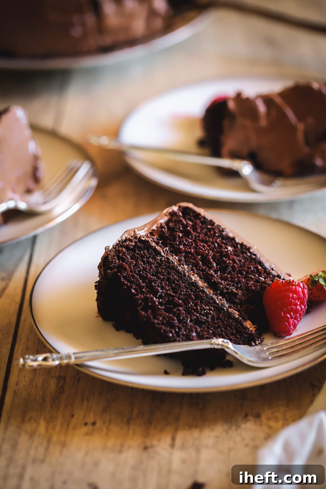 Three perfectly presented slices of Ina Garten's chocolate cake, also known as Beatty's chocolate cake, arranged on individual white plates, each accompanied by a gleaming silver fork. This inviting scene highlights the cake's delectable layers and irresistible appeal.
