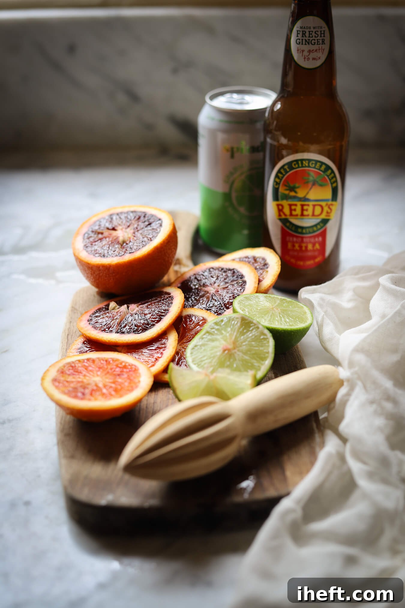 Ginger beer, lime spindrift, and slices of blood oranges and limes on a small cutting board. 