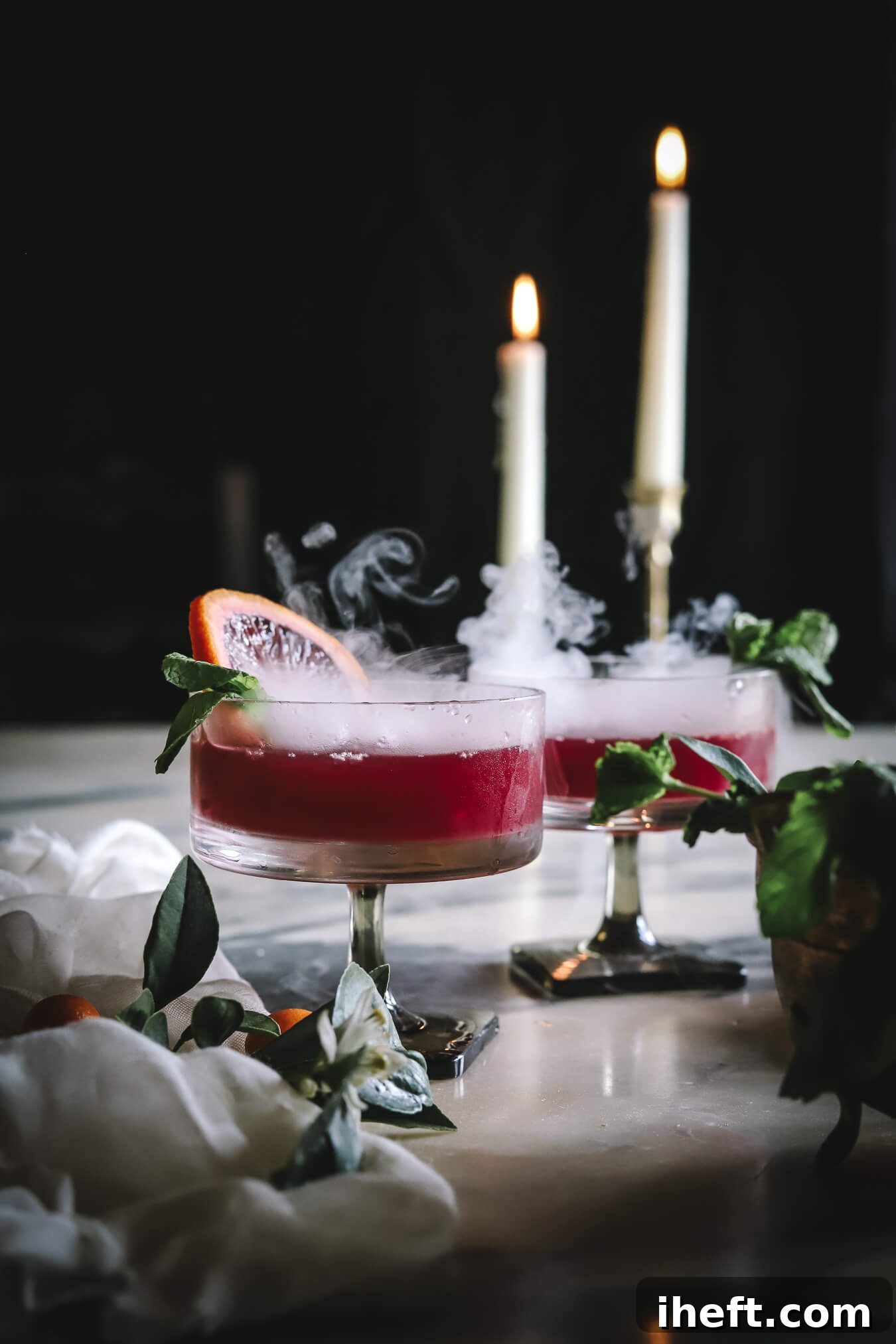Dark and moody drink food photography with dry ice. Two Halloween mocktails with dry ice. Two lit taper candles in the background. 