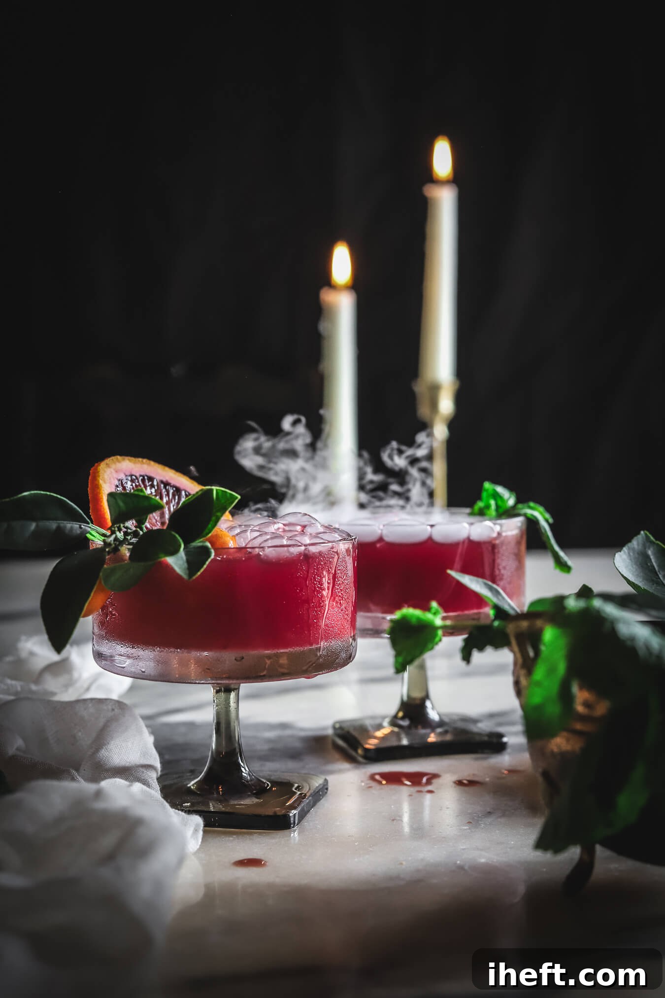 Two spooky easy red halloween drinks with blood orange slices and dry ice in vintage coupe glasses. 