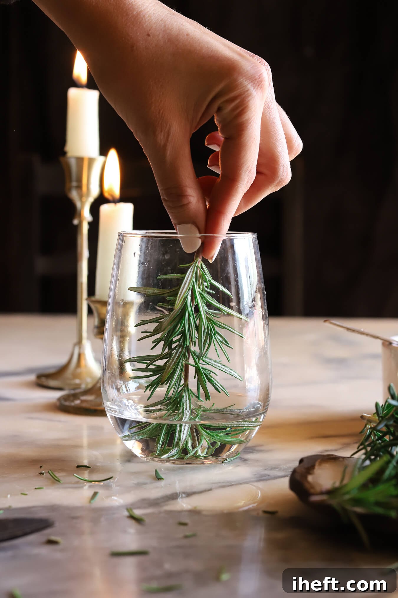 A sprig of rosemary is placed into a stemless wine glass to make a snow globe cocktail. 