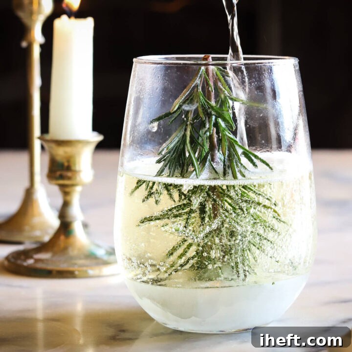 Champagne is poured into a stemless wine glass with a rosemary Christmas tree to make a snow globe Christmas cocktail.